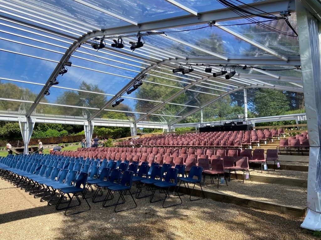 Seating area inside a temporary theatre marquee with transparent roof structure.