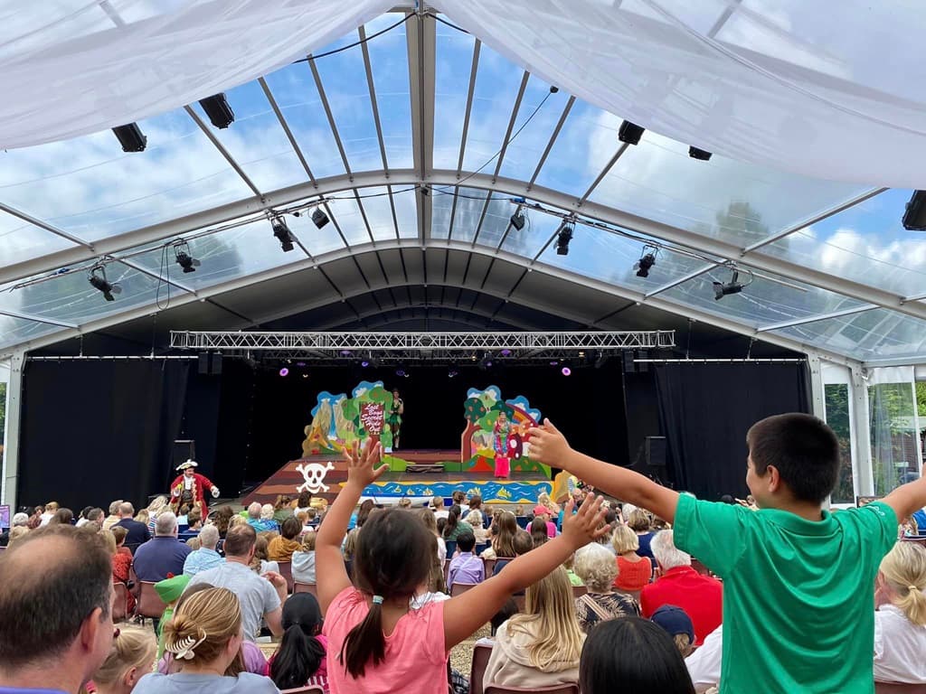 Audience watching a live performance inside a temporary theatre marquee with stage.